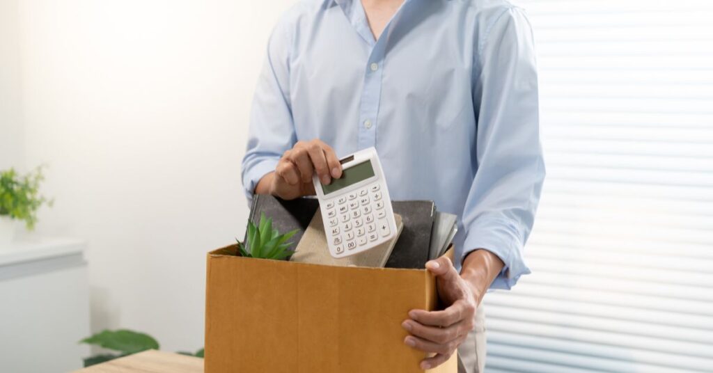 Persona empaquetando objetos personales de escritorio en una caja de cartón tras una desvinculación laboral, con una calculadora visible, representando el impacto de la automatización IA Chile en profesiones administrativas.